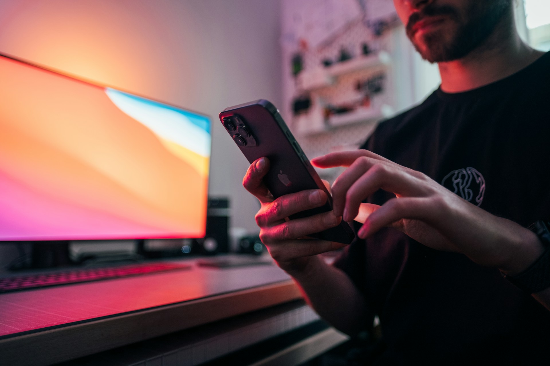 Man using a smartphone in front of a colourful monitor