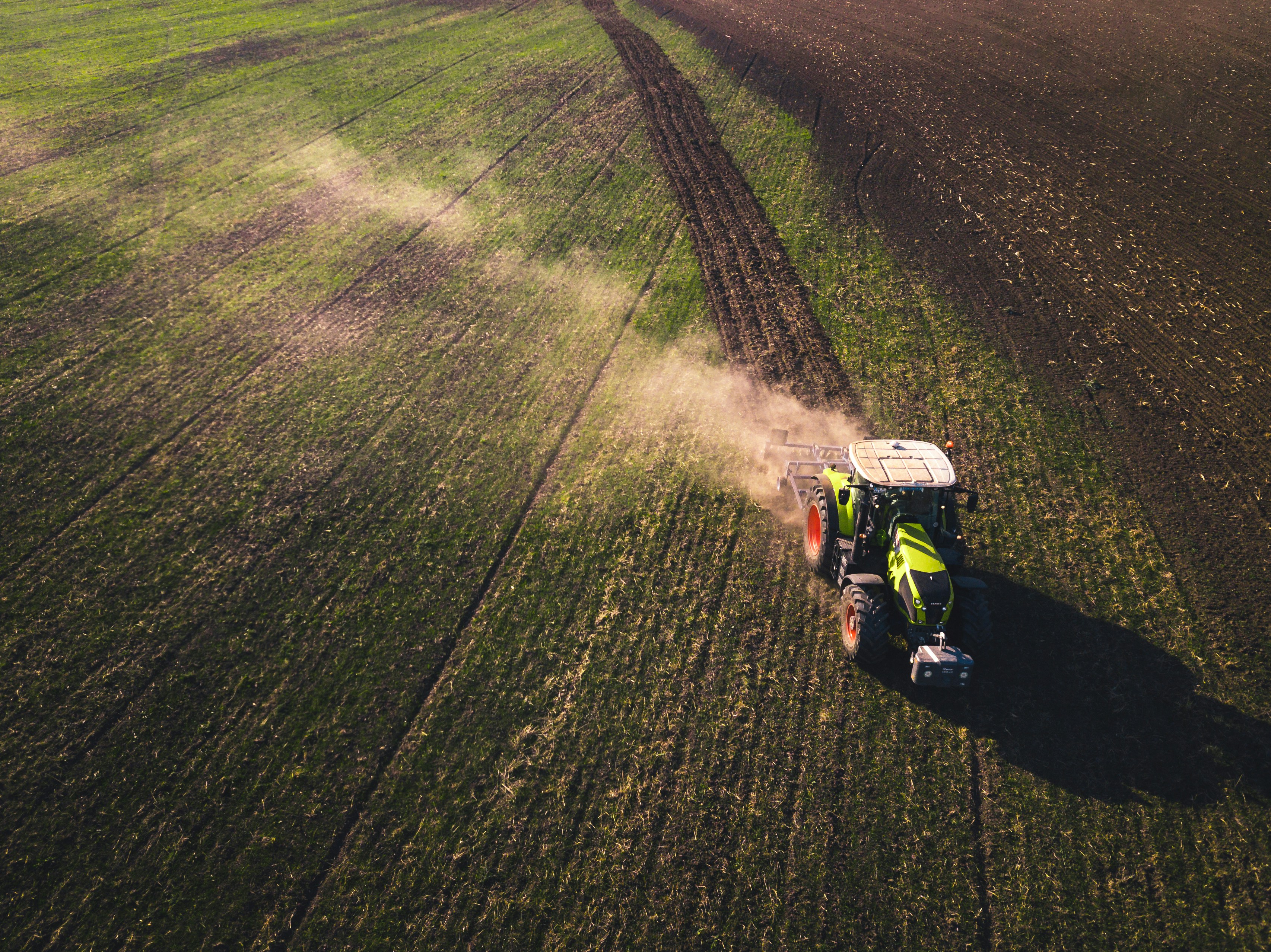 Aerial view of a tractor raising dust as it works a green field