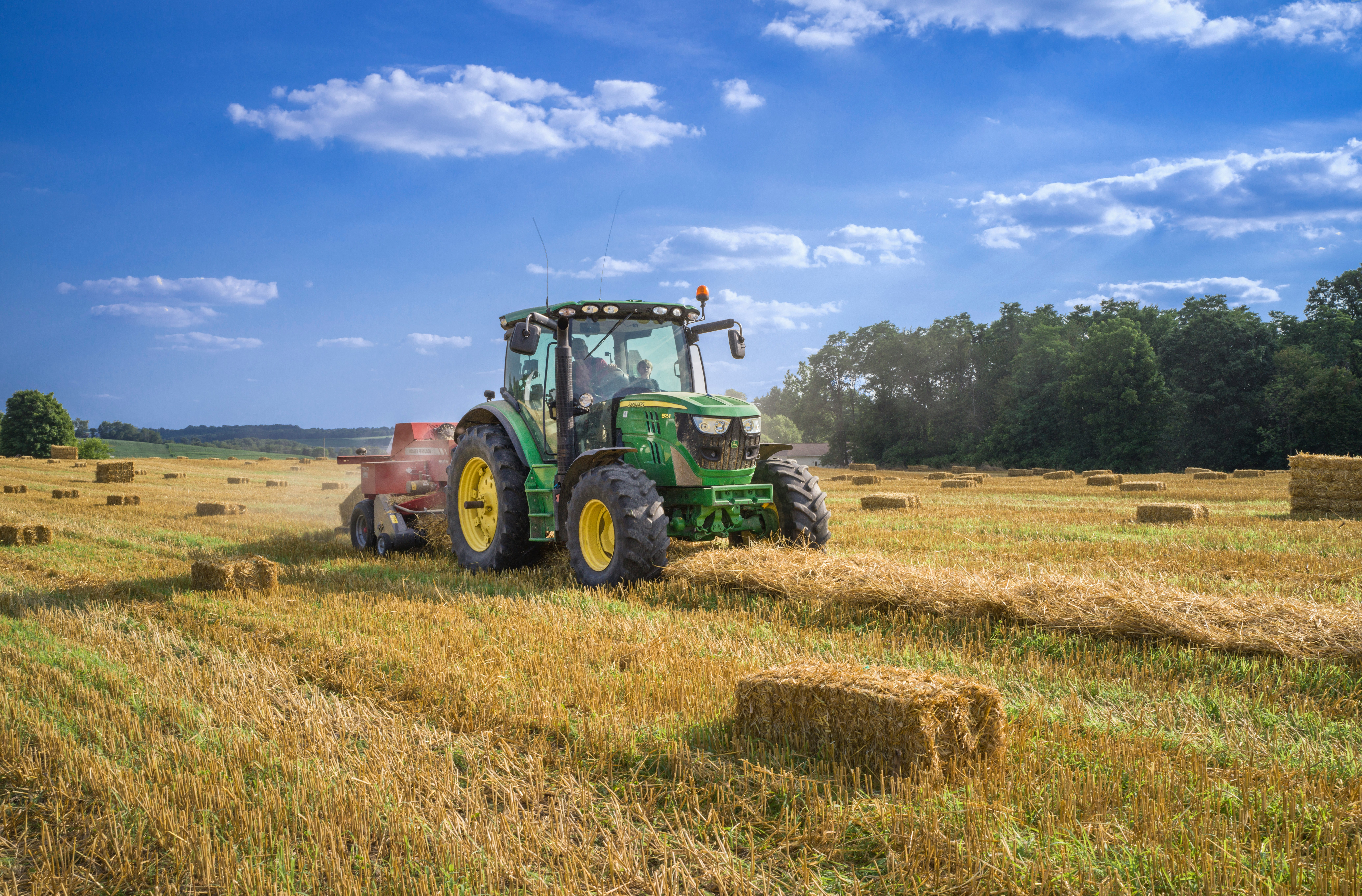 Green tractor baling straw in a harvested field