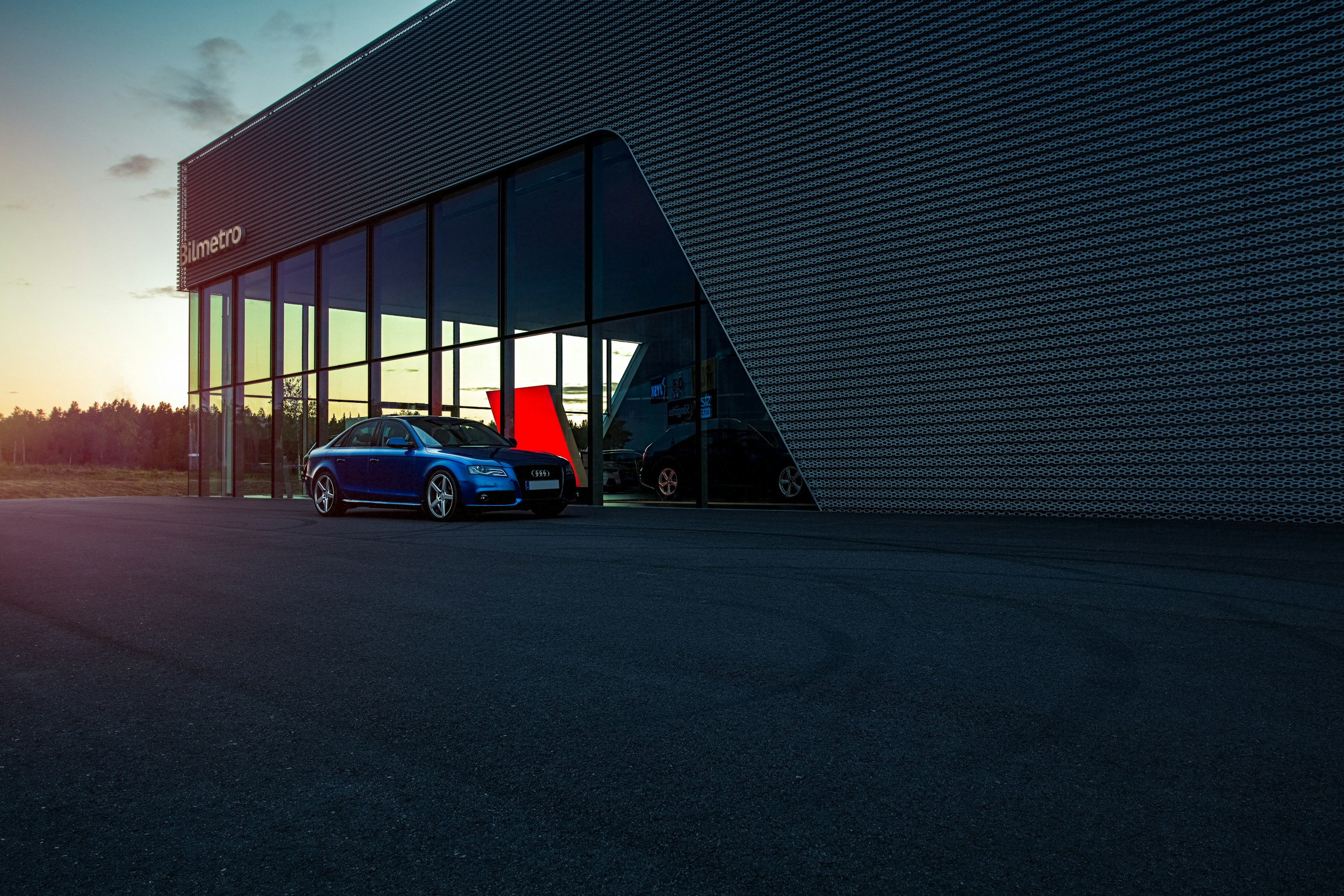 Blue saloon parked outside a glass-fronted car showroom at dusk