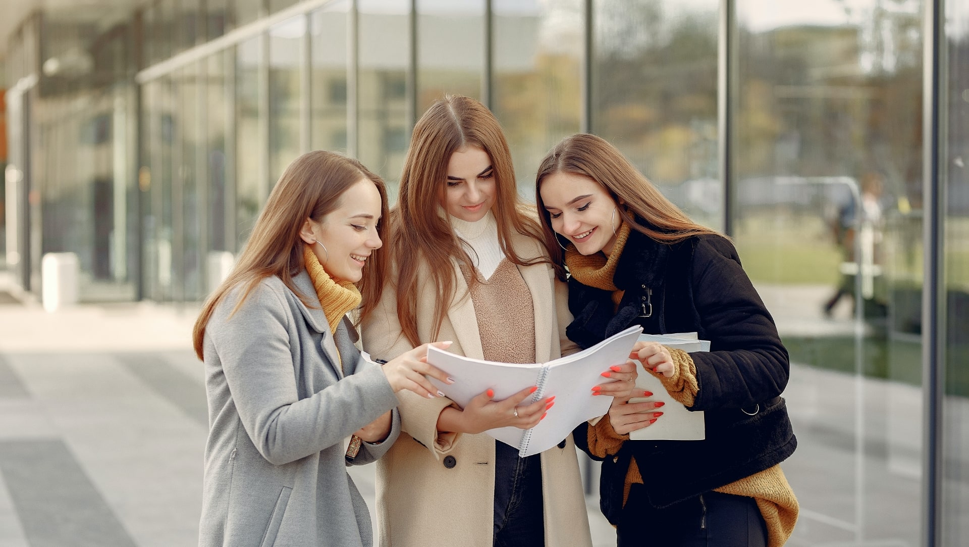 Three students looking through a folder together outside a building