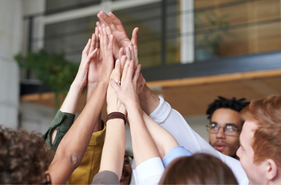Colleagues raising their hands together in an office