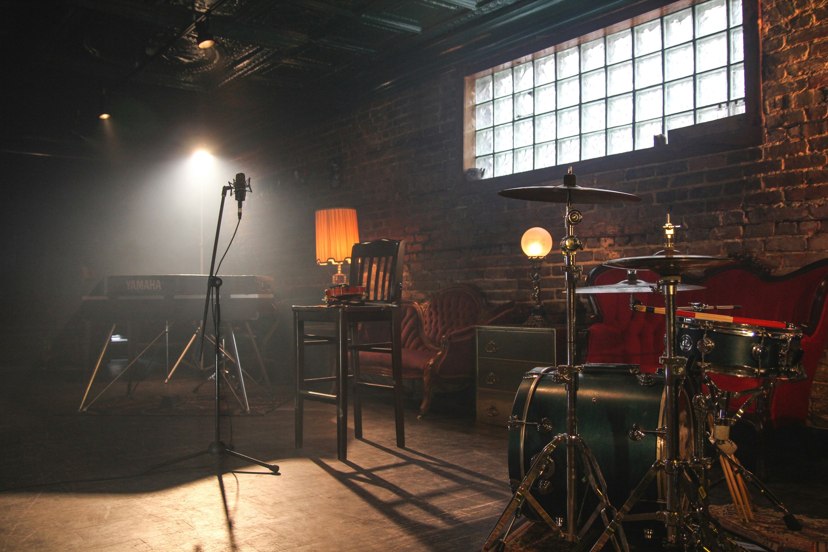 Drum kit, microphone and lamps in a dim brick-walled room