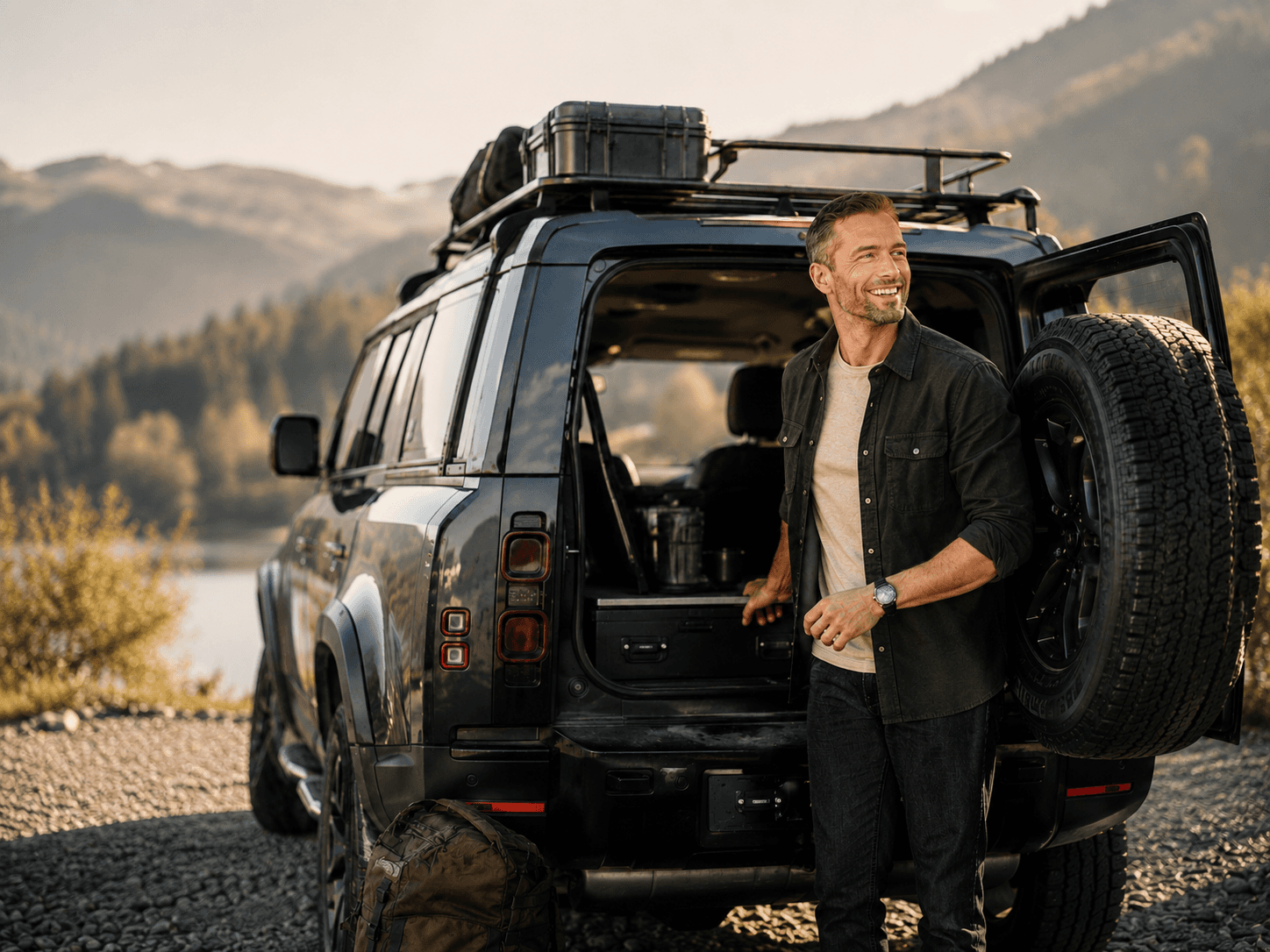Man standing at the open rear of an off-road vehicle by a lake