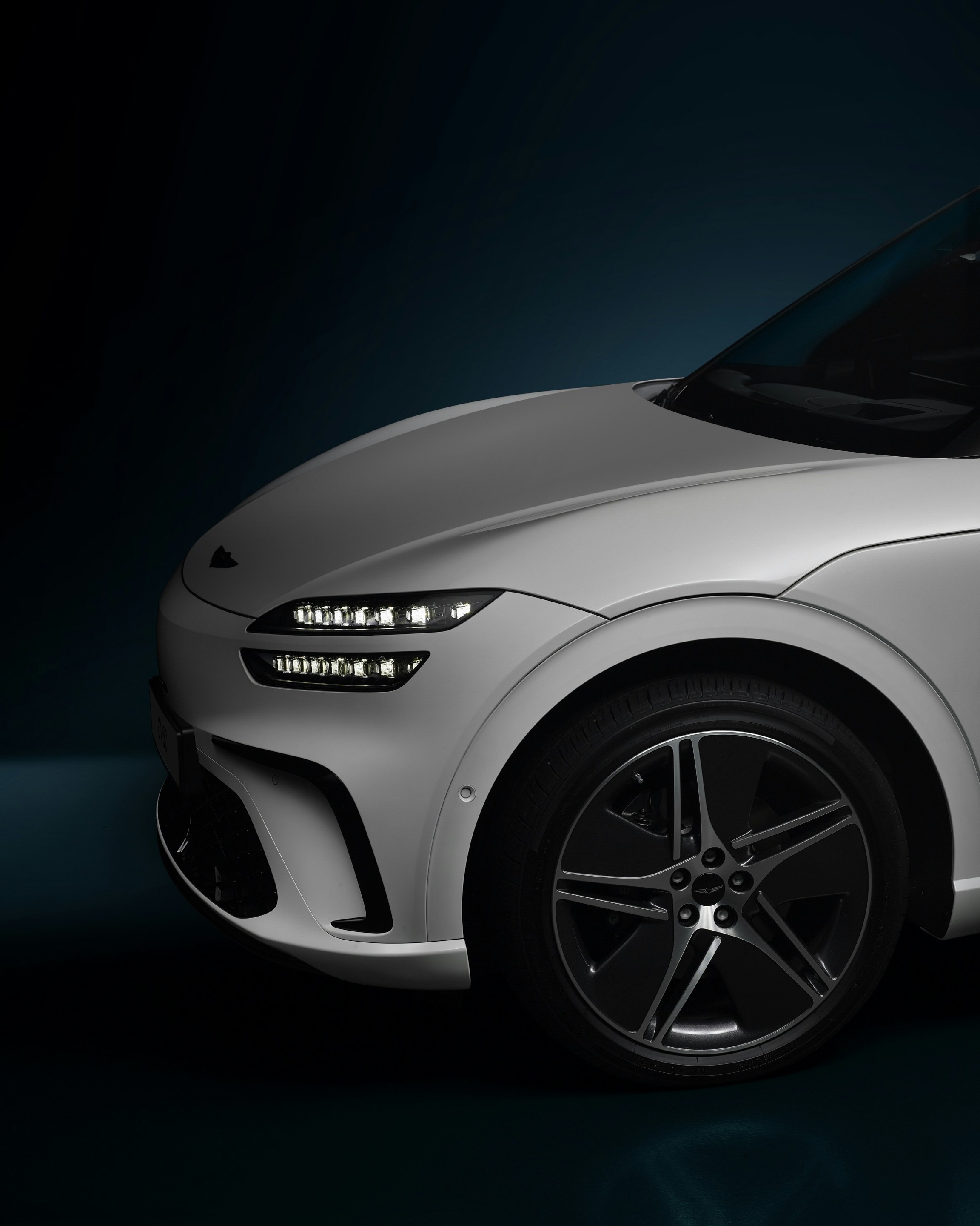 Front wheel and headlights of a silver car against a dark background