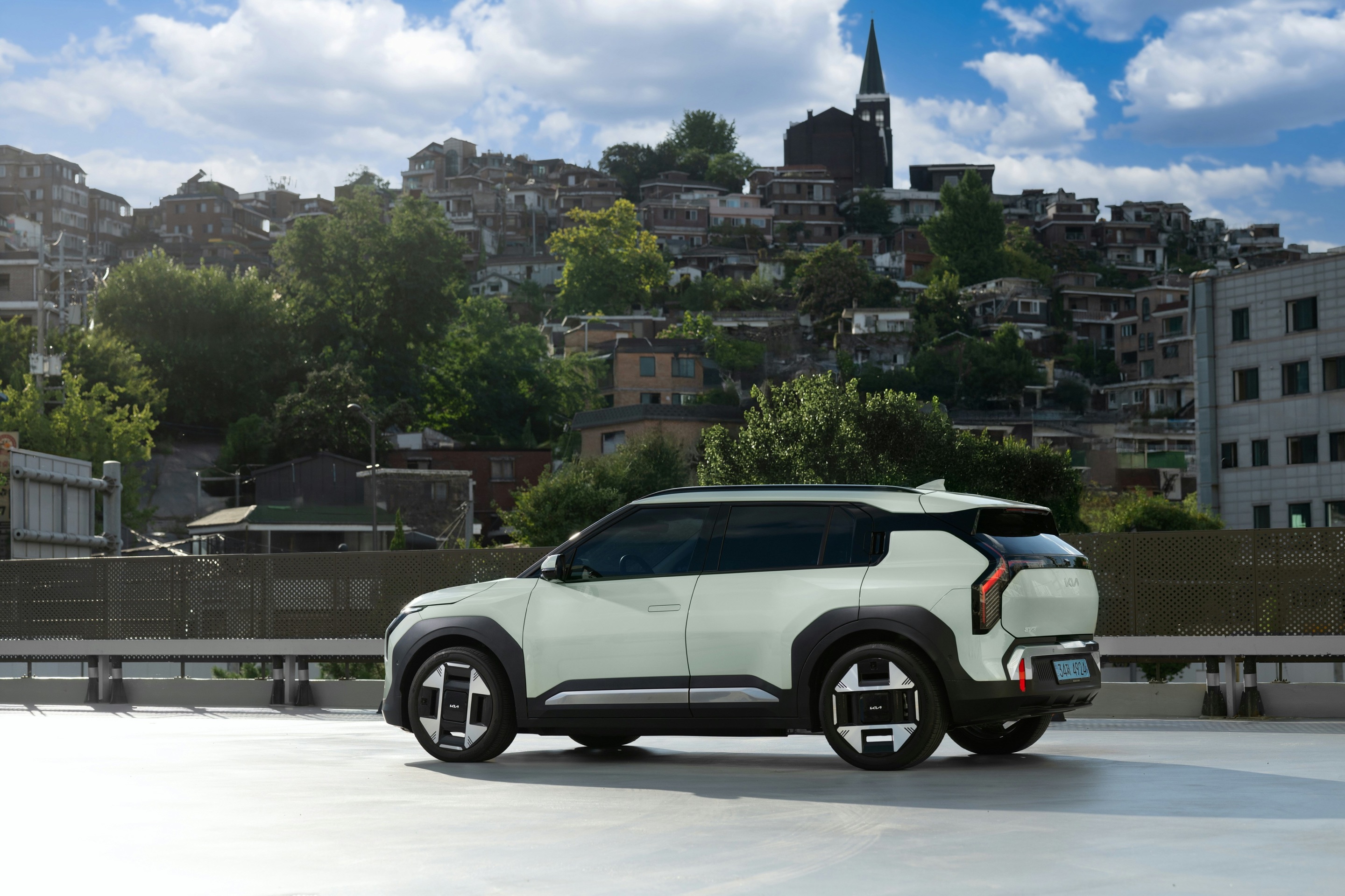 Pale green compact SUV on a rooftop above a hillside town
