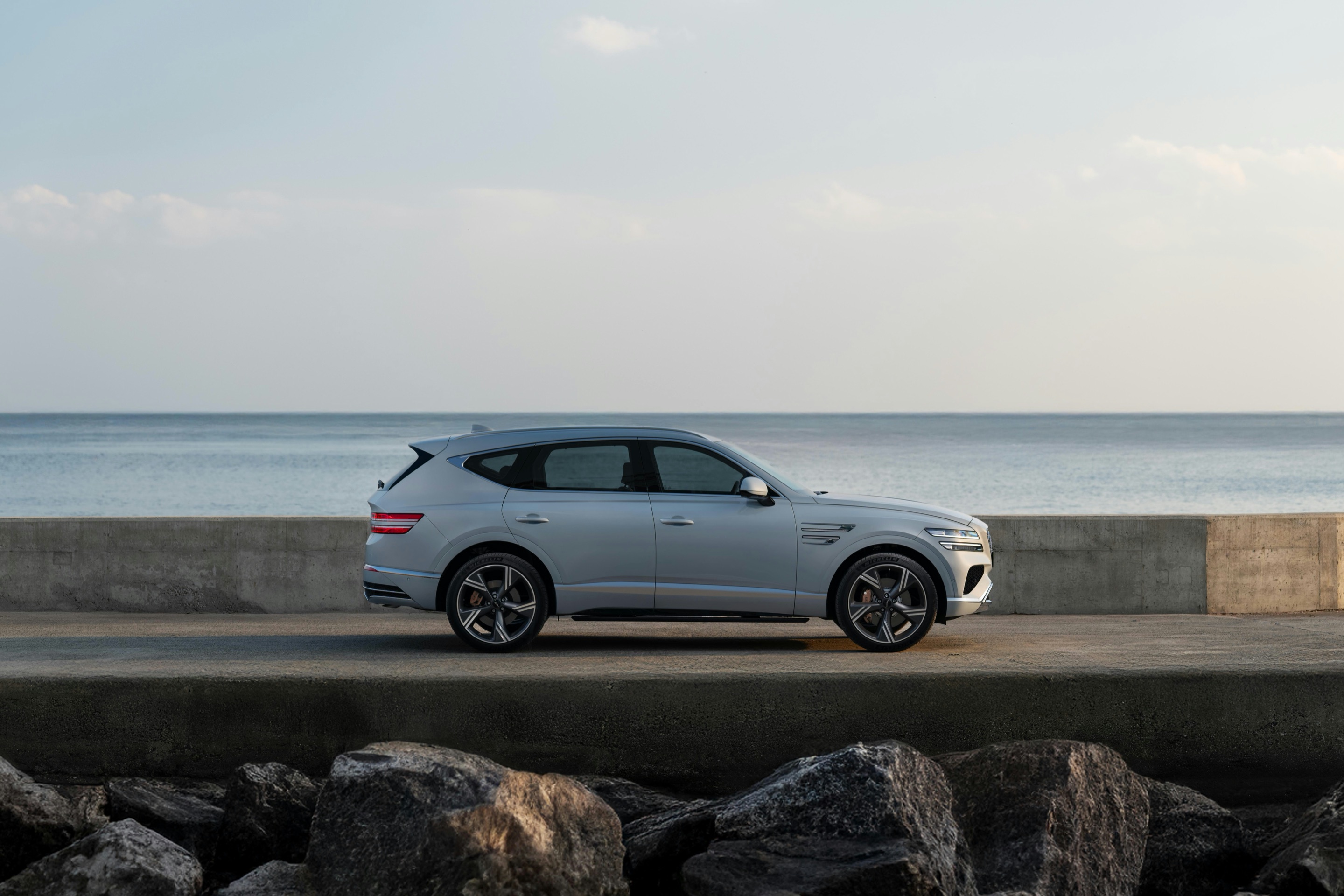 Silver SUV parked on a sea wall beside the water