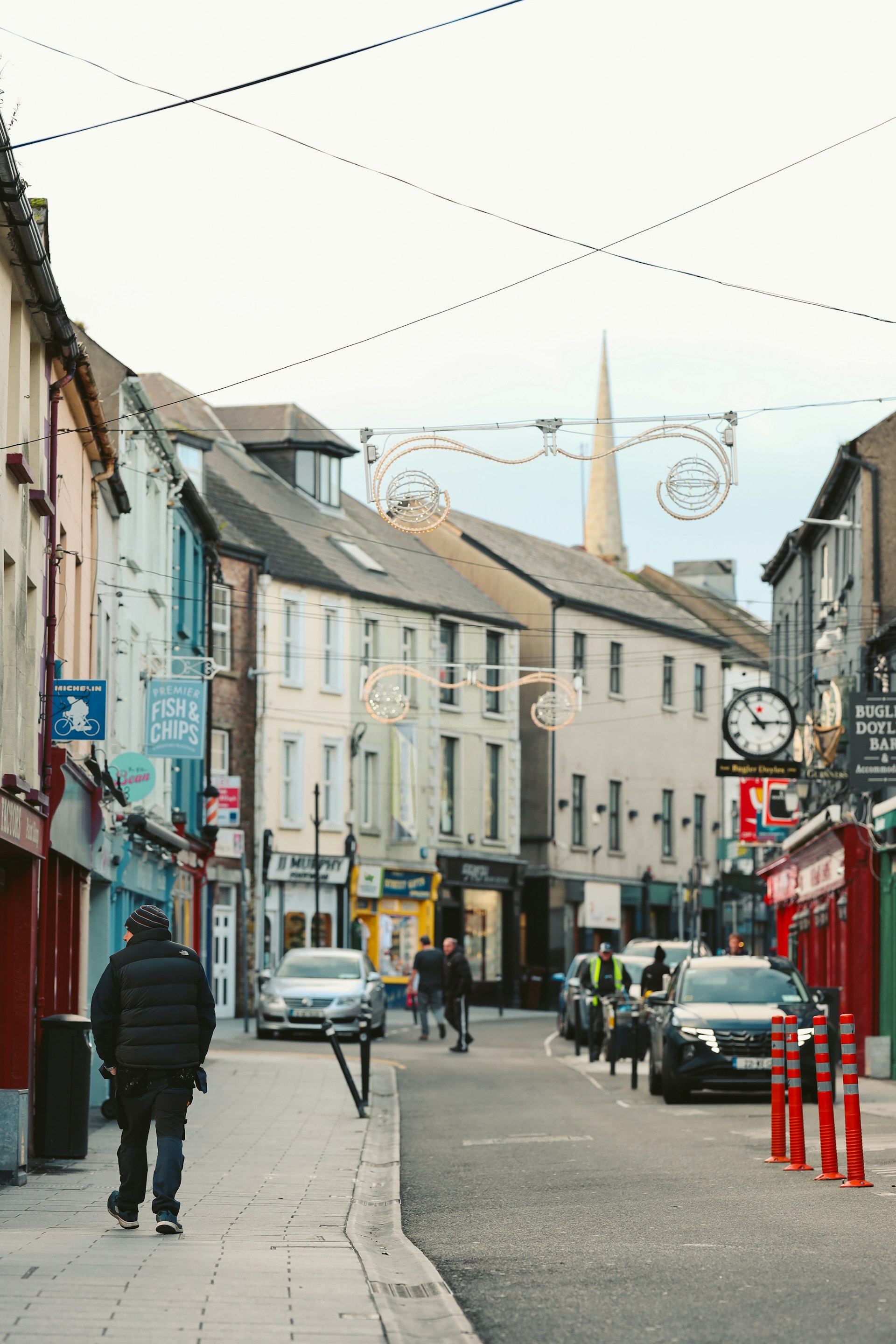 Shopfronts along a narrow town street with a church spire