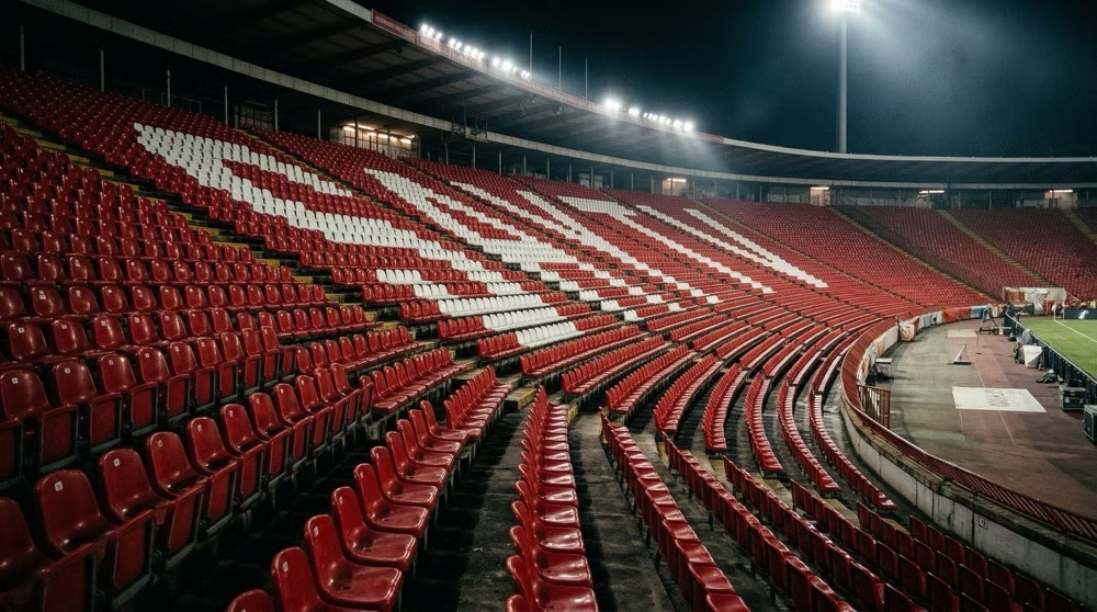 Empty red and white seats in a floodlit stadium at night